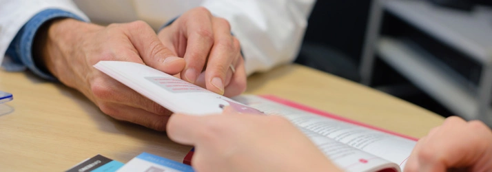 Close-up of two people reviewing printed brochures or documents on a wooden table, with one person pointing at a page and the other holding a booklet